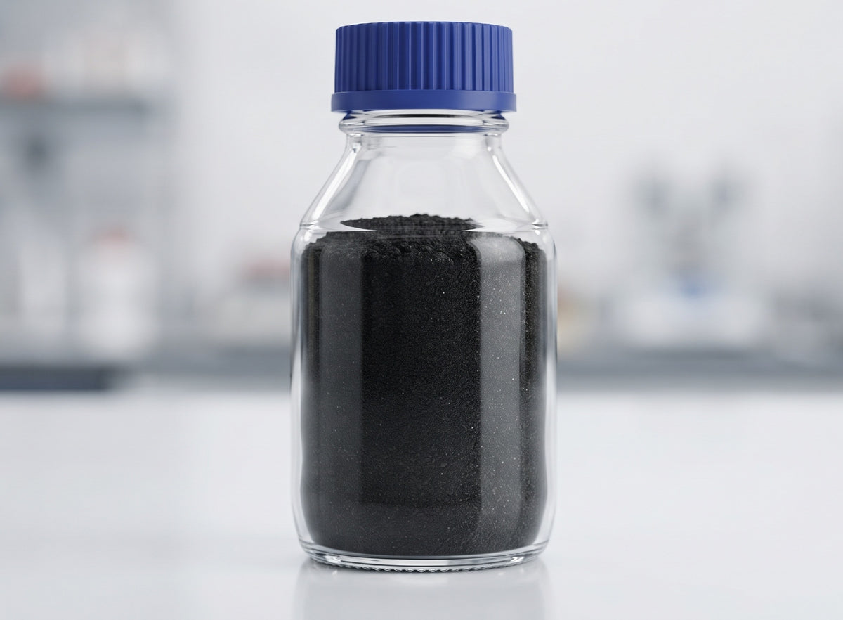 A clear glass bottle with a blue ribbed cap filled with black powder, set against a blurred light gray laboratory background.
